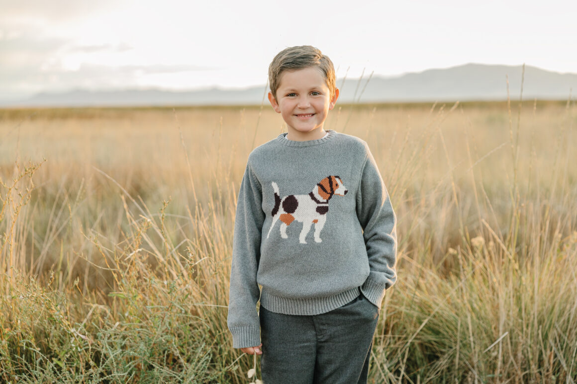 boy wearing a cozy sweater with a dog design, playing in a field. Comfortable boys and toddlers' sweater for active kids