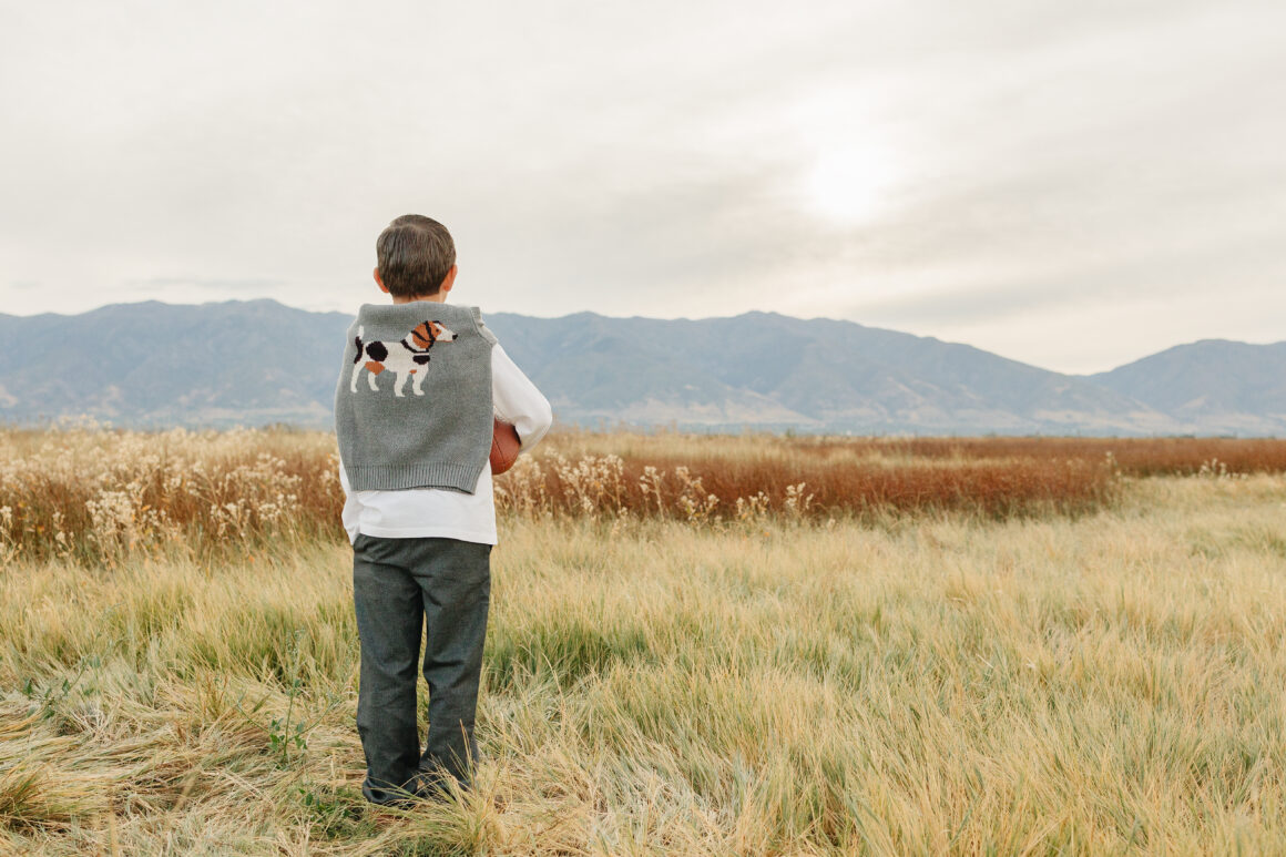 Young boy wearing premium organic cotton t-shirt, designer dress pants and luxury sweater draped around shoulders, showing casual-elegant style for toddlers and boys