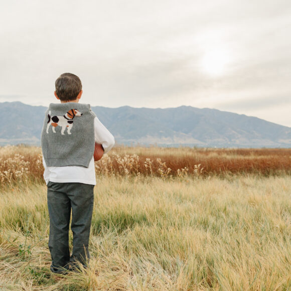 Young boy wearing premium organic cotton t-shirt, designer dress pants and luxury sweater draped around shoulders, showing casual-elegant style for toddlers and boys