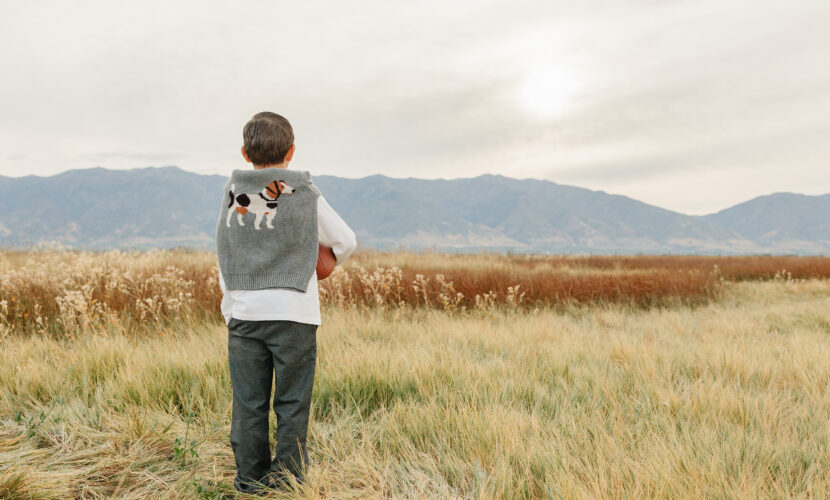 Young boy wearing premium organic cotton t-shirt, designer dress pants and luxury sweater draped around shoulders, showing casual-elegant style for toddlers and boys