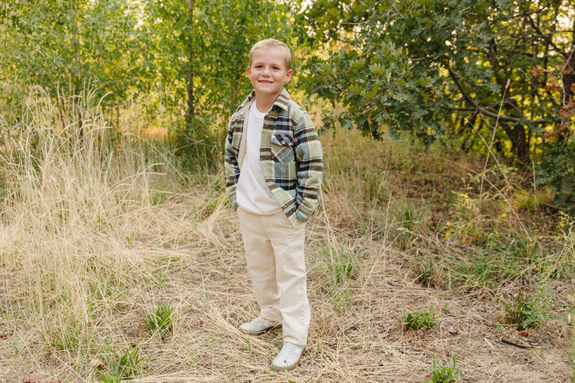 Boy wearing Chino-Flex boys dress pants in stone with plaid shacket and white tee outdoors